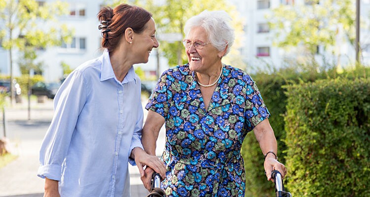 Eine fröhliche Mitarbeiterin und eine Bewohnerin spazieren zusammen und sind lachend in ein Gespräch vertieft.