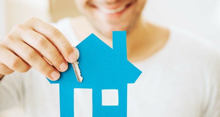 Mann welcher ein blaues Papierhaus und einen Haustürschlüssel in der Hand hält.